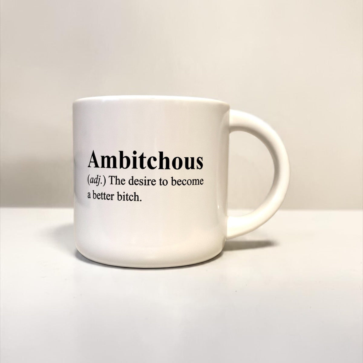 A white ceramic coffee mug with black printed text defining the word 'Ambitious' on a plain white background.