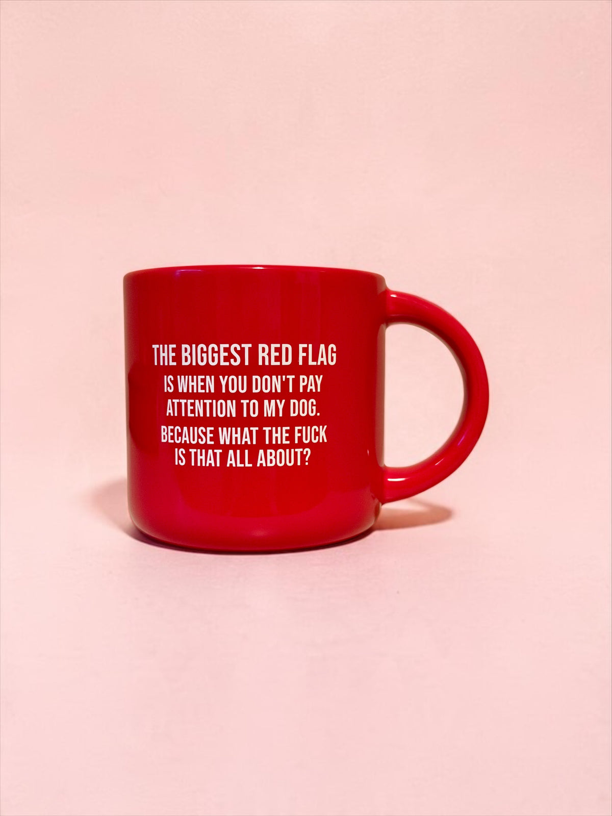 A glossy red ceramic mug with white printed text on a light pink background.